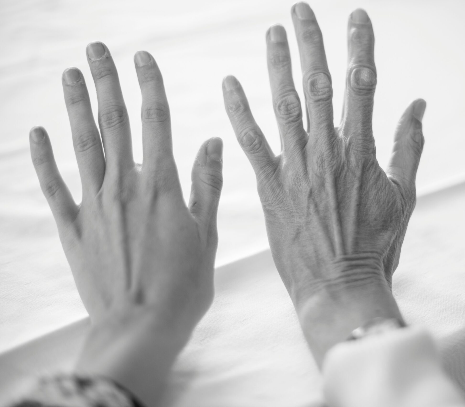 Two hands in black and white, one belonging to a young woman and one belonging to an elderly woman.