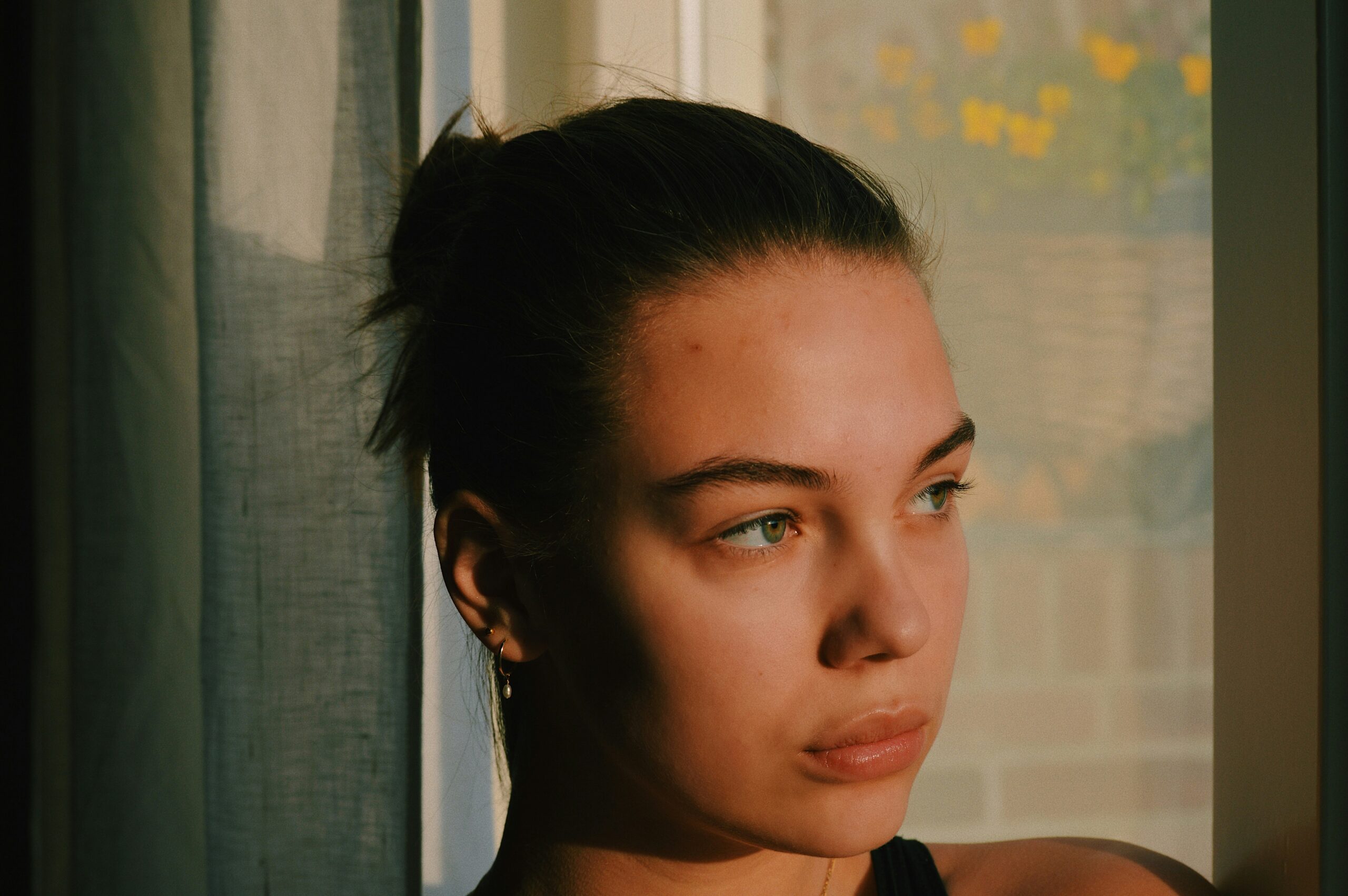 Woman with hair in bun in front of a green curtain in the sun.