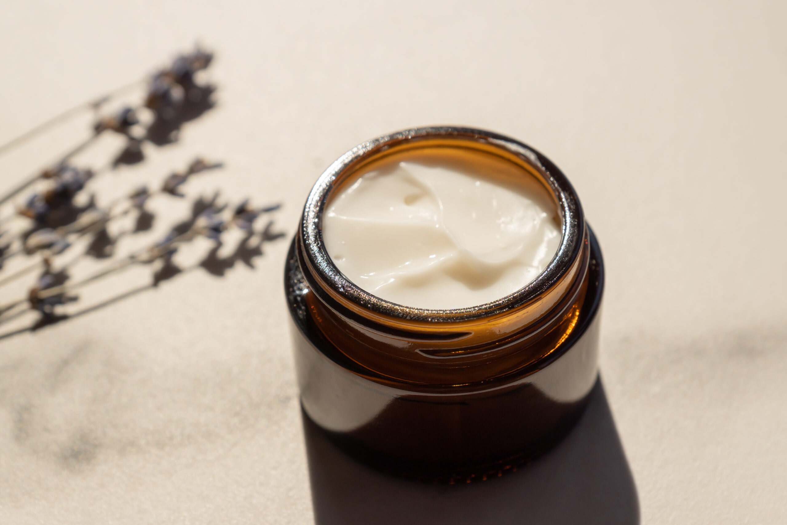 dark glass jar with cream, flowers of dried purple lavender blossom on marble table.